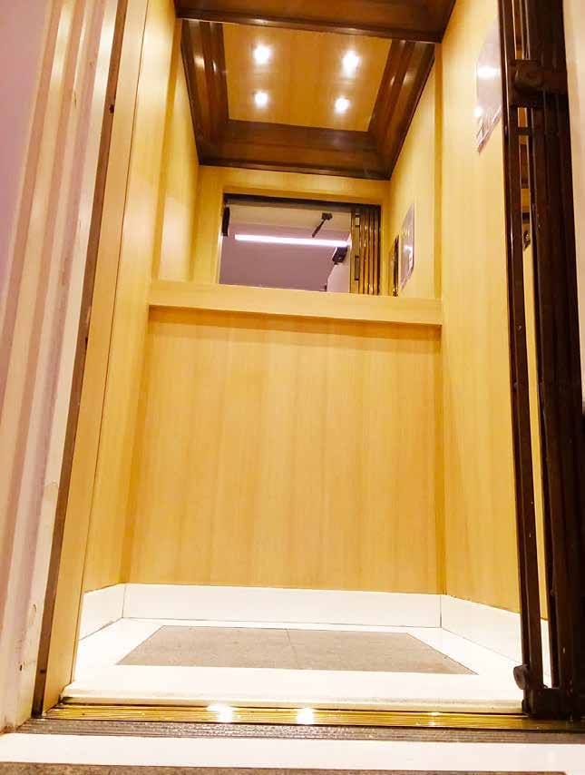 Projeto customizado de cabina de elevador em madeira clara com subteto recortado e iluminação embutida