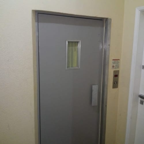 Porta de pavimento de elevador antes da reforma: pintura desgastada, batente sem acabamento e visor riscado